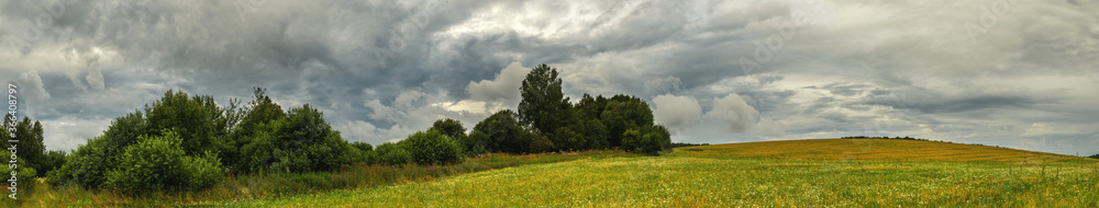 Extra wide panorama of green hills and trees on the edge of field.Cloudy spring or summer panoramic rural landscape. Extra wide panorama of green hills and trees on the edge of field.Cloudy spring or summer panoramic rural landscape.