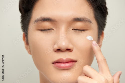 Portrait of satisfied young man applying facial cream isolated over white background