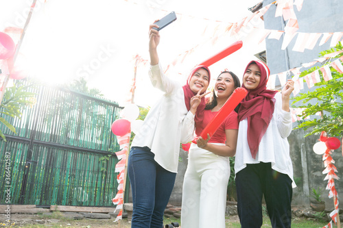 having fun a group of asian girls taking a selfie together on Indonesian Independence Day celebrations in the field with balloons and small red and white decorations