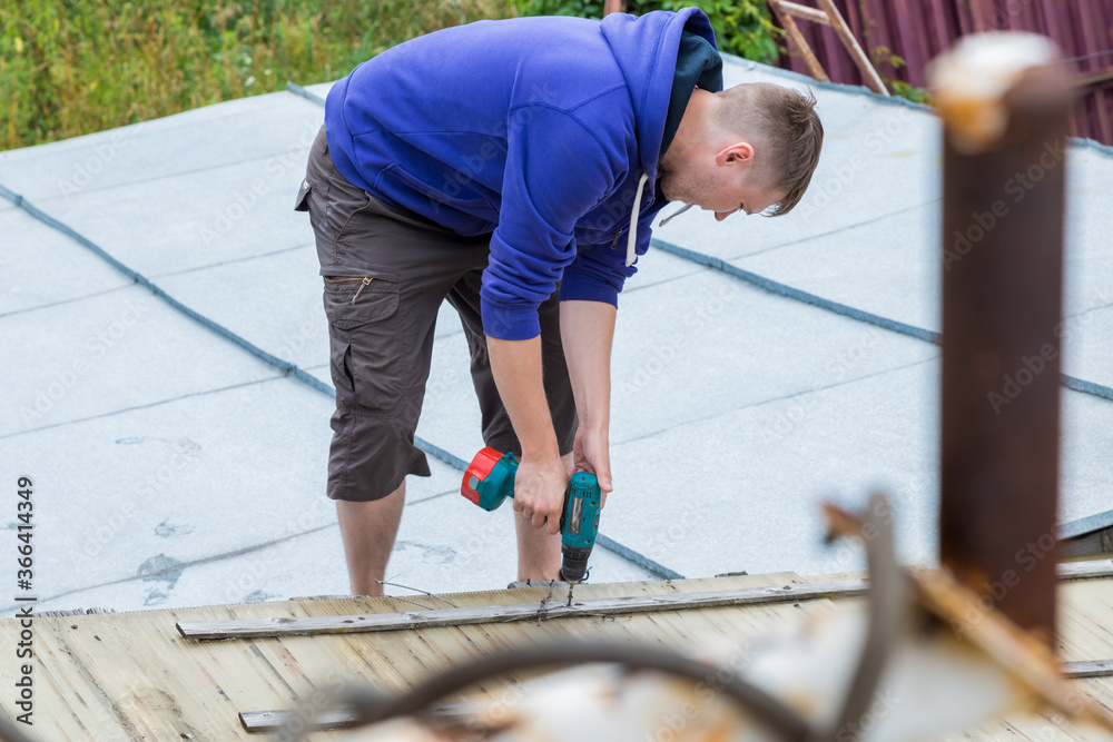 A man holds a screwdriver in his hands while standing on the roof A man holds a screwdriver in his hands while standing on the roof