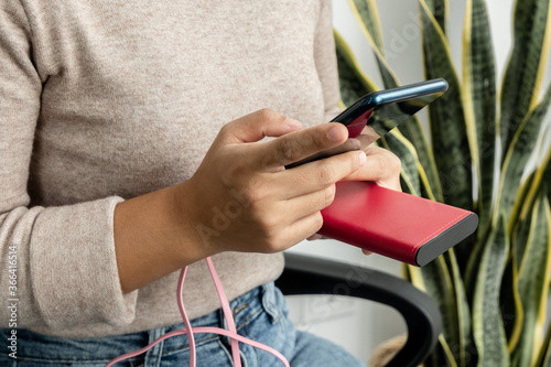 The hand of a young woman holding a smart phone and a modern backup battery charger Charge your smartphone with a backup battery, In size sit play on chair