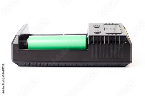 A black charger for two 18650 batteries. A green and brown 18650 battery on a white background next to the discharge, on charging. Male hand puts the battery on charge
