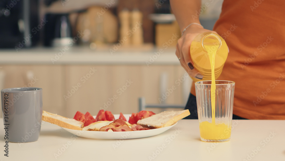 Woman pouring fresh juice in glass for breakfast in kitchen. Woman drinking healthy and natural orange juice. Housewife drinking healthy, natural, homemade orange juice. Refreshing sunday morning