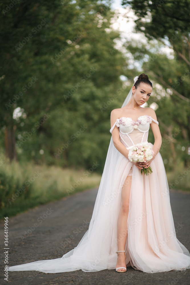 Gorgeous bride in elegant wedding dress stand in linden alley with bouquet and posing to photographer Gorgeous bride in elegant wedding dress stand in linden alley with bouquet and posing to photographer