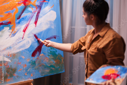 Woman with painting brush creating a masterpiece on large canvas. Modern artwork paint on canvas, creative, contemporary and successful fine art artist drawing masterpiece