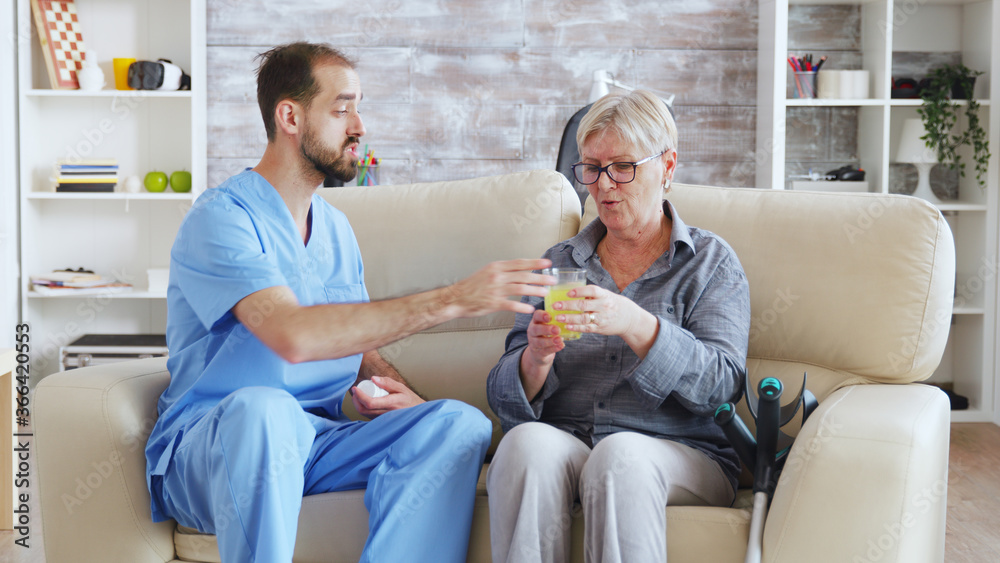 Male nurse sitting on couch with senior woman giving her medical treatment in nursing home.