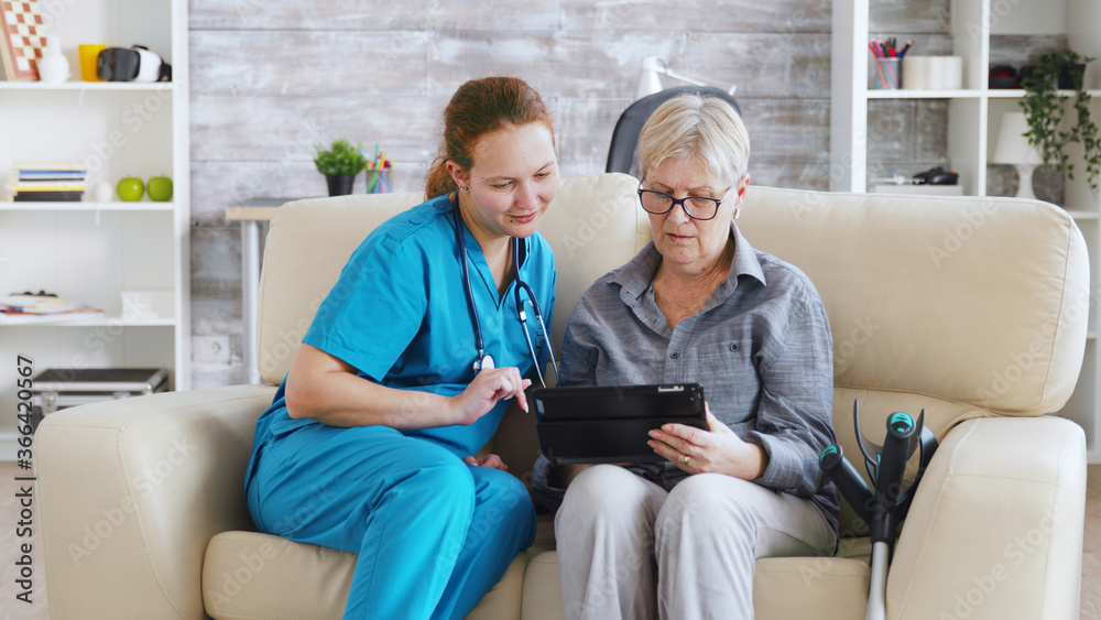 Female nuse helping senior elderly retired woman how to use her tablet computer in nursing home Female nuse helping senior elderly retired woman how to use her tablet computer in nursing home