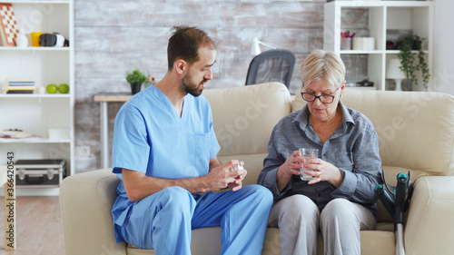 Bilde på lerret Male nurse sitting on couch with senior woman giving her medical treatment in nursing home