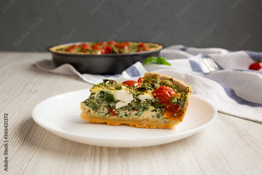 A Piece of Homemade Spinach Quiche on a white plate, side view. Close-up.
