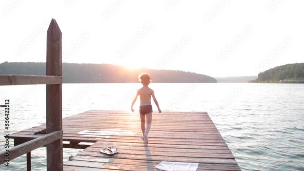 A boy jumps from a pier into the sea or lake in the mountains on warm sunny summer day. A boy jumps from a pier into the sea or lake in the mountains on warm sunny summer day.