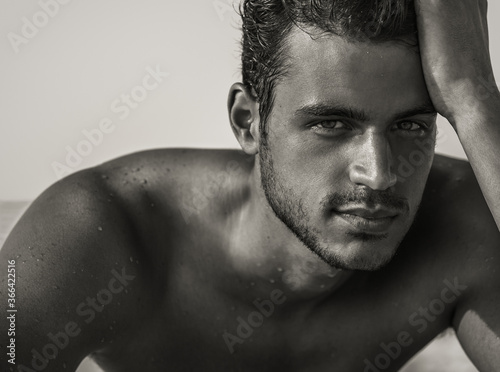 Sexy closeup portrait of handsome topless male model on the beach with beautiful eyes staring into the camera. Black and White beauty.