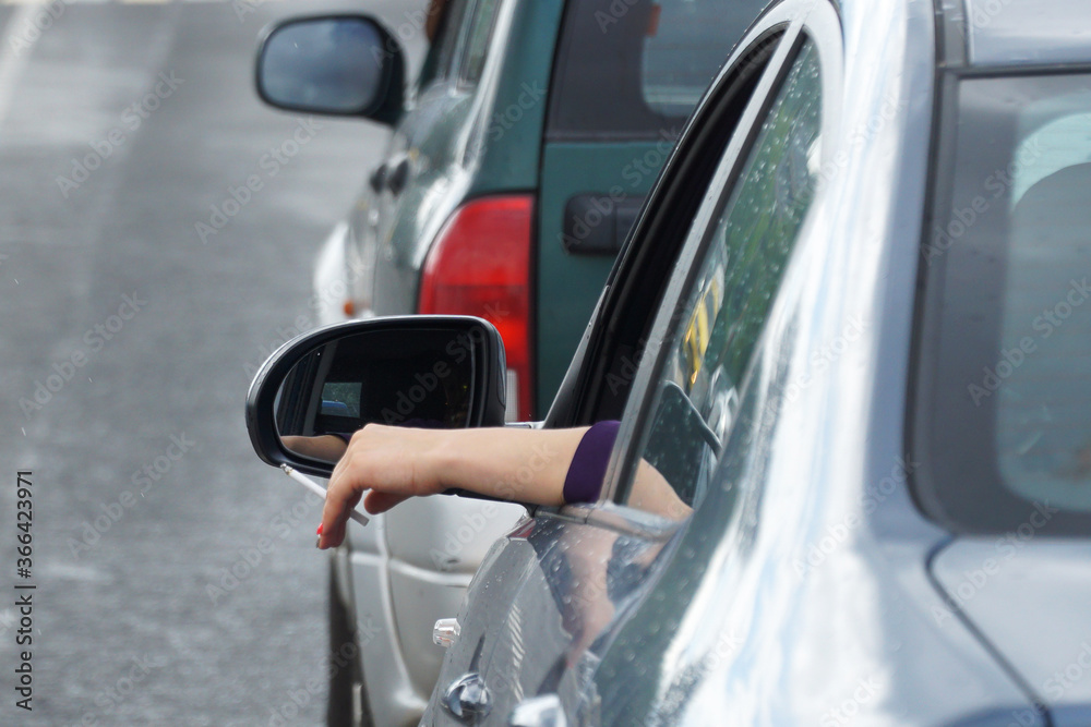 A woman's hand with a cigarette sticks out of the front window of the car.