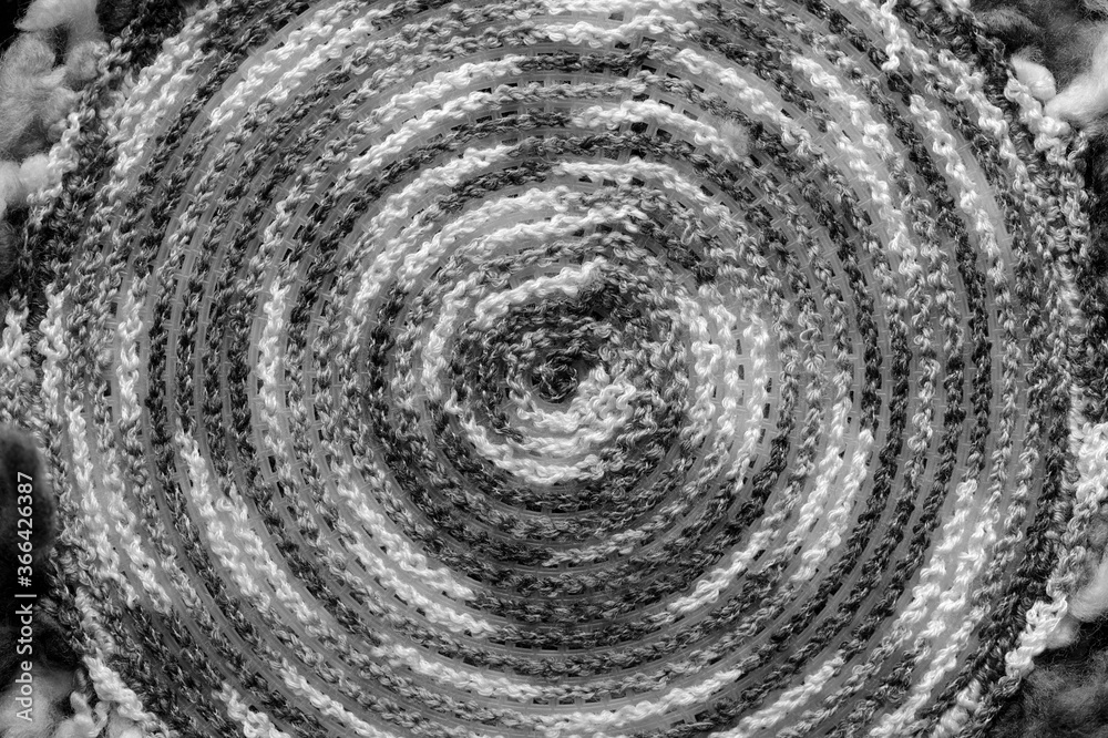 Fragment of a crocheted circle from melange threads based on a plastic canvas from the wrong side close-up. Black and white