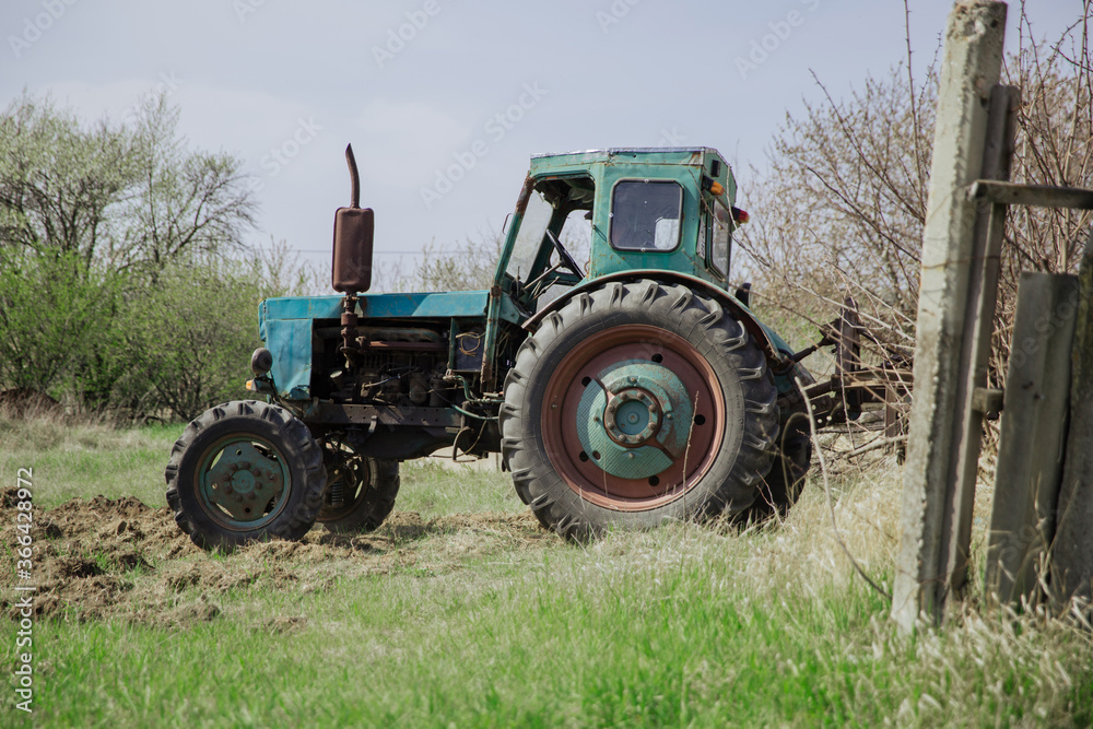 An old blue tractor plows a field and cultivates the soil. Agriculture. An old blue tractor plows a field and cultivates the soil. Agriculture.