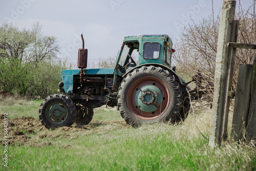 An old blue tractor plows a field and cultivates the soil. Agriculture.