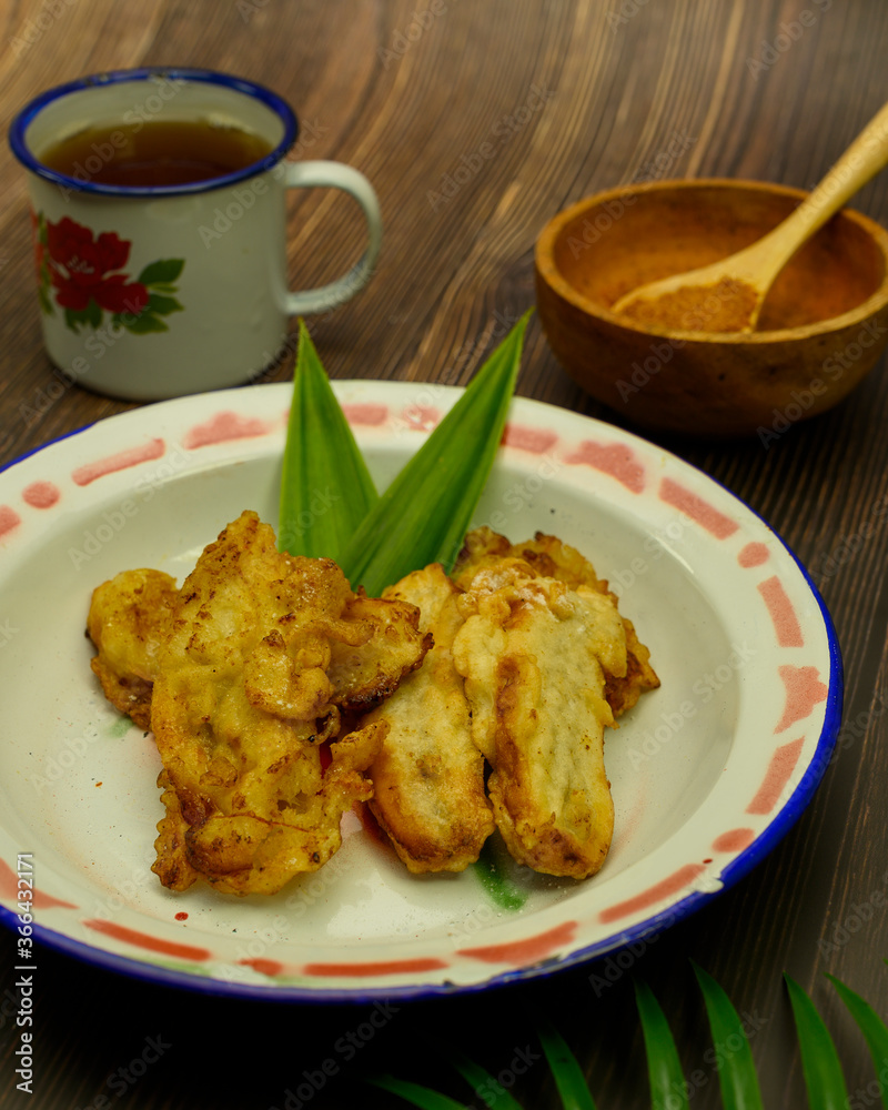 Indonesian traditional food of fried banana with pandan leaves served in a metal plate with palm sugar powder and a cup of hot tea Indonesian traditional food of fried banana with pandan leaves served in a metal plate with palm sugar powder and a cup of hot tea