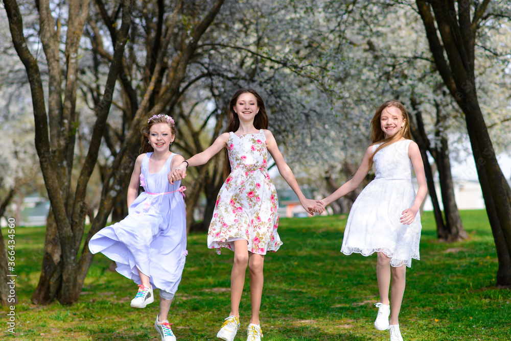 Naklejka premium Three beautiful girls in retro dresses for a walk in a flowered garden. The idea and concept of a friendly family and a happy childhood.