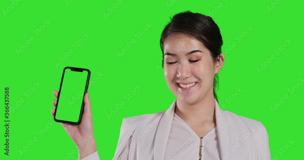 Portrait of business woman showing smartphone to camera with smile at green screen background. Portrait shot at green screen studio. Portrait of business woman showing smartphone to camera with smile at green screen background. Portrait shot at green screen studio.