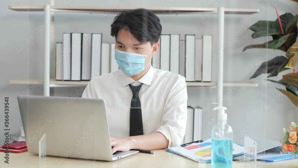 Asian business man wearing face masks working in office with table shield partition and alcohol gel to protect coronavirus covid-19, social distancing and new normal life concept. Asian business man wearing face masks working in office with table shield partition and alcohol gel to protect coronavirus covid-19, social distancing and new normal life concept.