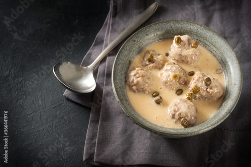 Boiled meatballs in a white bechamel sauce with capers, called Koenigsberger Klopse, traditional Polish and German dish in bowl on a dark gray background with copy space, view from above photo