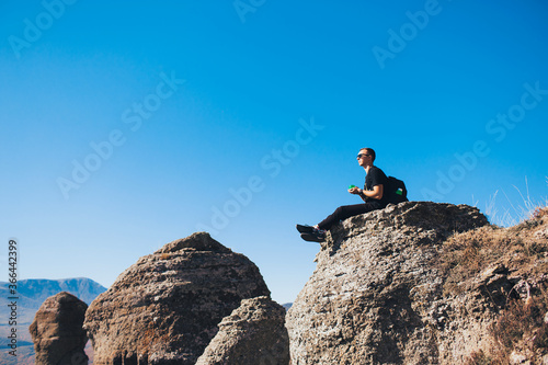 A guy with a backpack sits on a rock in the mountains and enjoying view of nature. Nature background. Journey. A trip to the mountains.