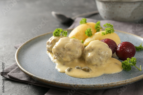 Koenigsberger Klopse or meatballs in a white bechamel sauce with capers, potatoes and beetroot served on a gray blue plate, traditional Polish and German dish, copy space, selected focus photo
