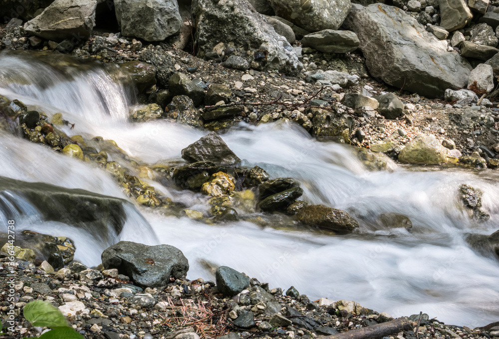 Water stream flowing between rocks into the forest. Water spring in Bucegi National Park. Water stream flowing between rocks into the forest. Water spring in Bucegi National Park.