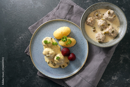 Koenigsberger Klopse or meatballs in white sauce with capers, potatoes and beetroot served in a bowl and on a gray blue plate, dark rustic background with copy space, high angle view from above photo