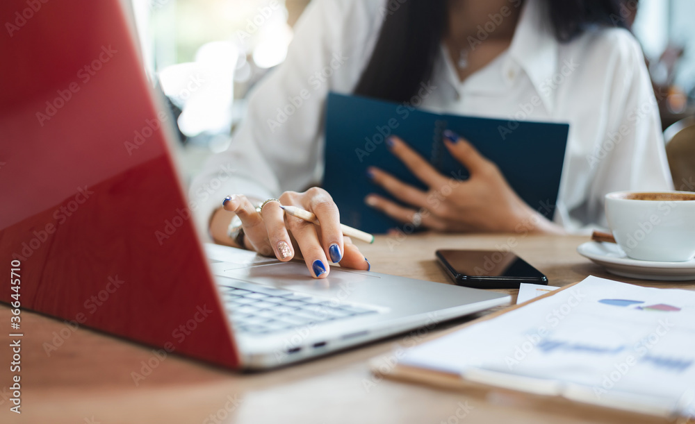 Close-up of hand businesswoman using computer laptop and smart phone working with paperwork of investment on desk Close-up of hand businesswoman using computer laptop and smart phone working with paperwork of investment on desk