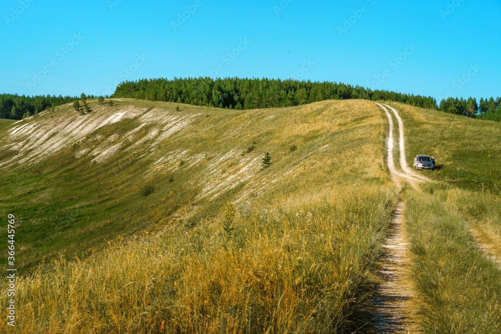 Winding gravel road between fields leads to hills to natural hills is natural dusty sun clouds green field Winding gravel road between fields leads to hills to natural hills is natural dusty sun clouds green field
