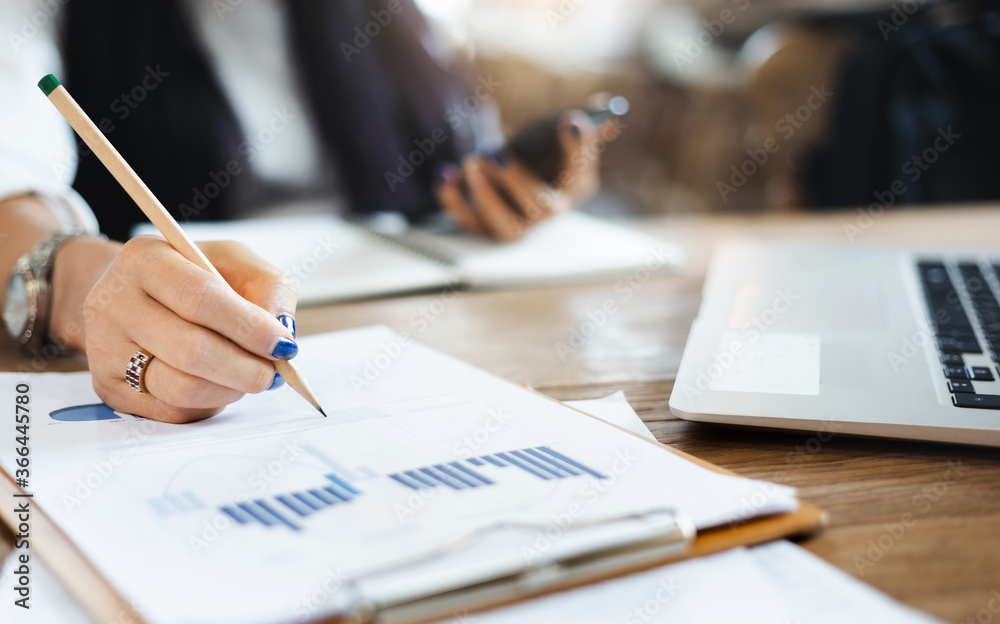 Close-up of hand businesswoman writing on paperwork of investment while she working with computer laptop and smart phone