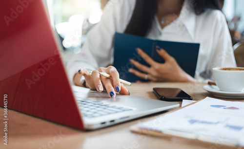 Close-up of hand businesswoman using computer laptop and smart phone working with paperwork of investment on desk