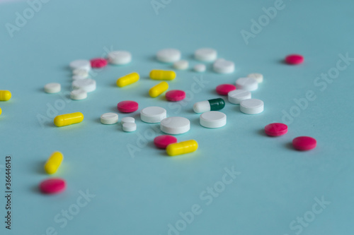 Tablets of different shapes and colors are scattered randomly. White, yellow, pink. Medical concept on blue background, pharmacy theme.