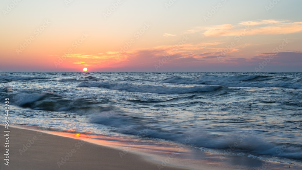Obraz premium Beautiful sunset at the sea with rough waves on a hot, summer evening.
