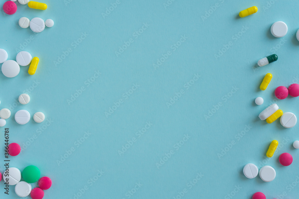 Tablets of different shapes and colors lie chaotically on the left and right sides. Medical concept on a blue background, pharmacy. Empty space for text. Copy space