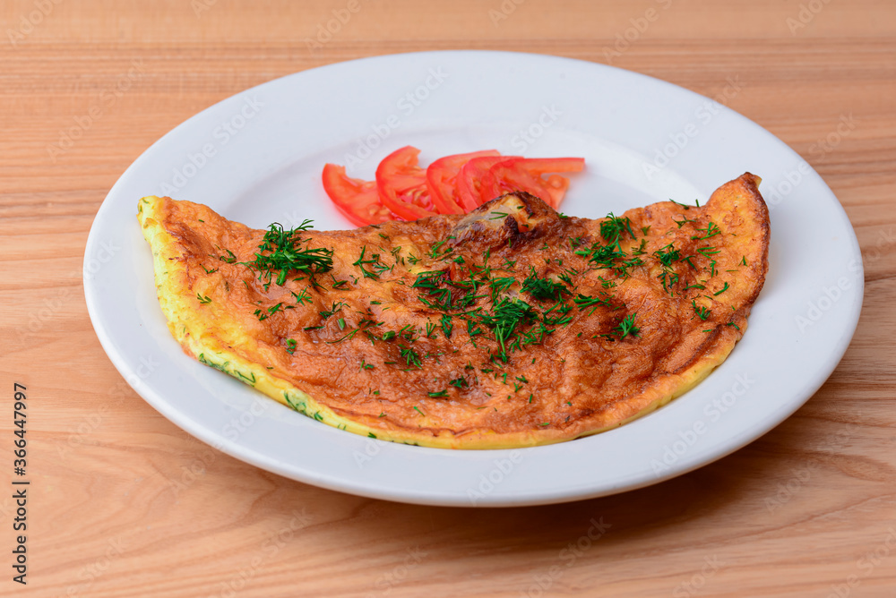 Delicious egg omelette with greens and tomatoes. Served on a white plate over light rustic wooden table background.