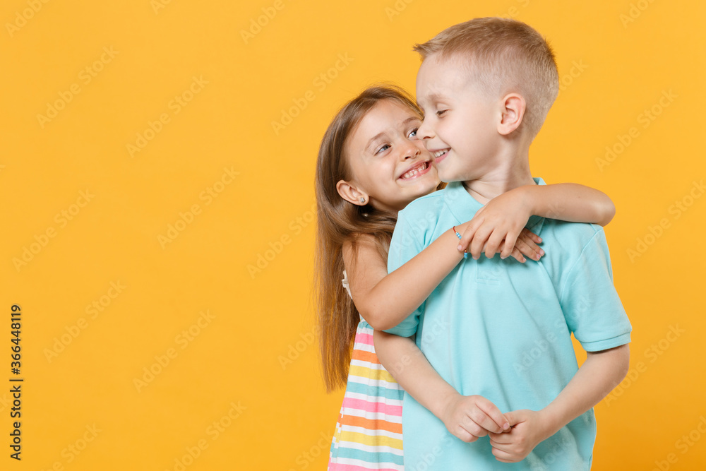 Little couple kids boy girl 5-6 years old in blue pink clothes shirt dress posing have fun isolated on yellow background children studio portrait. People childhood lifestyle concept embrace hug love