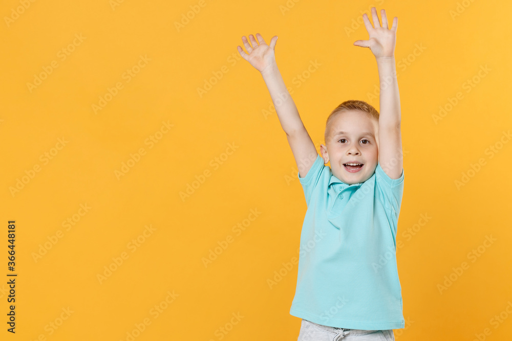 Smiling little fun male kid boy 5-6 years old in blue t-shirt polo posing raised hands up isolated on yellow background children studio portrait. People childhood lifestyle concept. Mock up copy space Smiling little fun male kid boy 5-6 years old in blue t-shirt polo posing raised hands up isolated on yellow background children studio portrait. People childhood lifestyle concept. Mock up copy space
