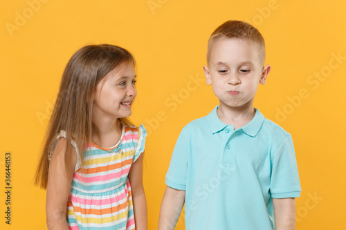 Little couple boy girl 5-6 years old in blue pink clothes shirt dress have fun isolated on yellow background children studio portrait. People lifestyle concept pointing index fingers on blowing cheeks