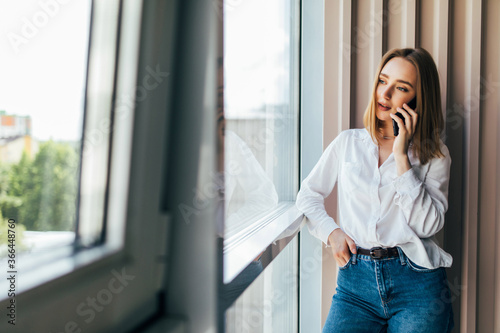 Beautiful young business woman sitting at office desk and talking on phone © dianagrytsku