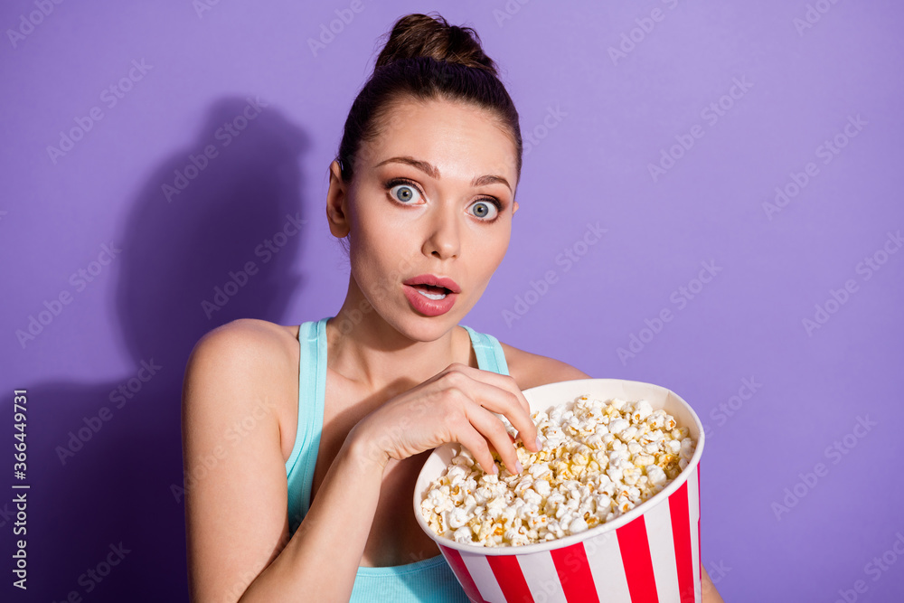 Portrait of astonished girl have free time eat big pop corn box watch tv impressed series open mouth wear singlet isolated over purple color background