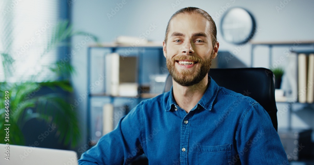 Obraz premium Close up of cheerful handsome Caucasian man putting off medical mask and smiling to camera while sitting at office. Happy male employee in good mood in cabinet indoors. Portrait concept