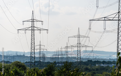 High voltage lines and power pylons in a green landscape against a gray sky background.