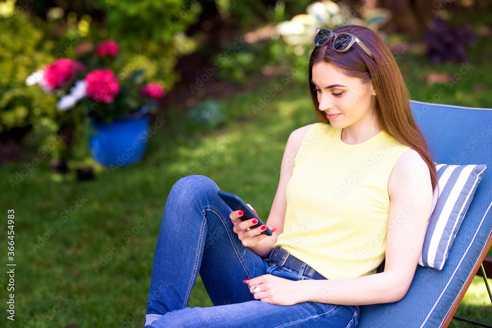 Beautiful young woman relaxing and text messaging in the garden at home Beautiful young woman relaxing and text messaging in the garden at home