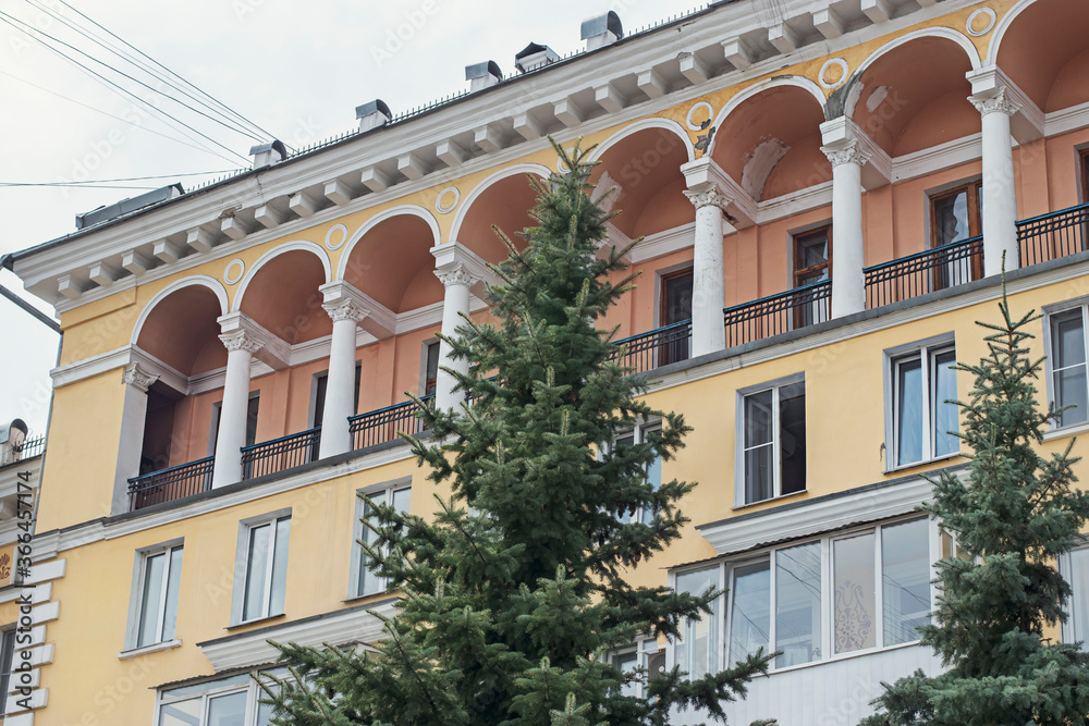 Fototapeta premium A multi-storey building with columns and carved balconies on a cloudy summer day, in the Russian province. The architectural heritage of the USSR of the twentieth century.