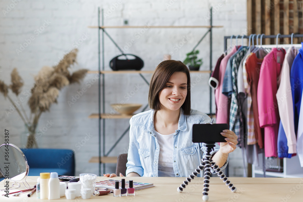 Vlogger turn on camera on mobile phone and broadcast live video to social network at home.Young female blogger recording a tutorial video for her beauty blog about cosmetics. Blogging, makeup concept.