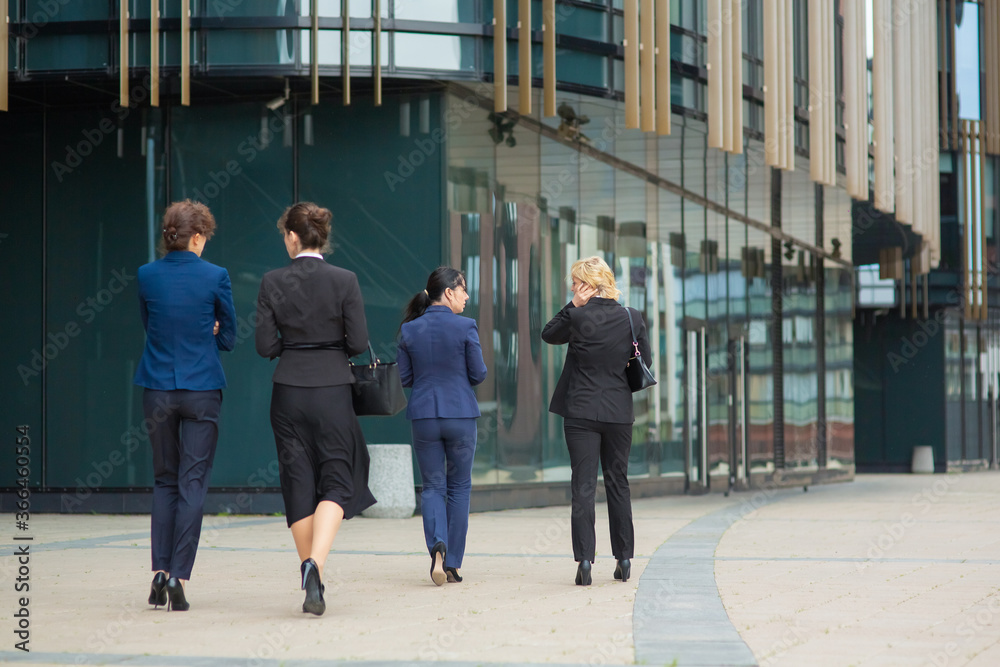 Back view of business ladies walking together outdoors, going to office building, talking, discussing project. Full length, rear view. Work break concept