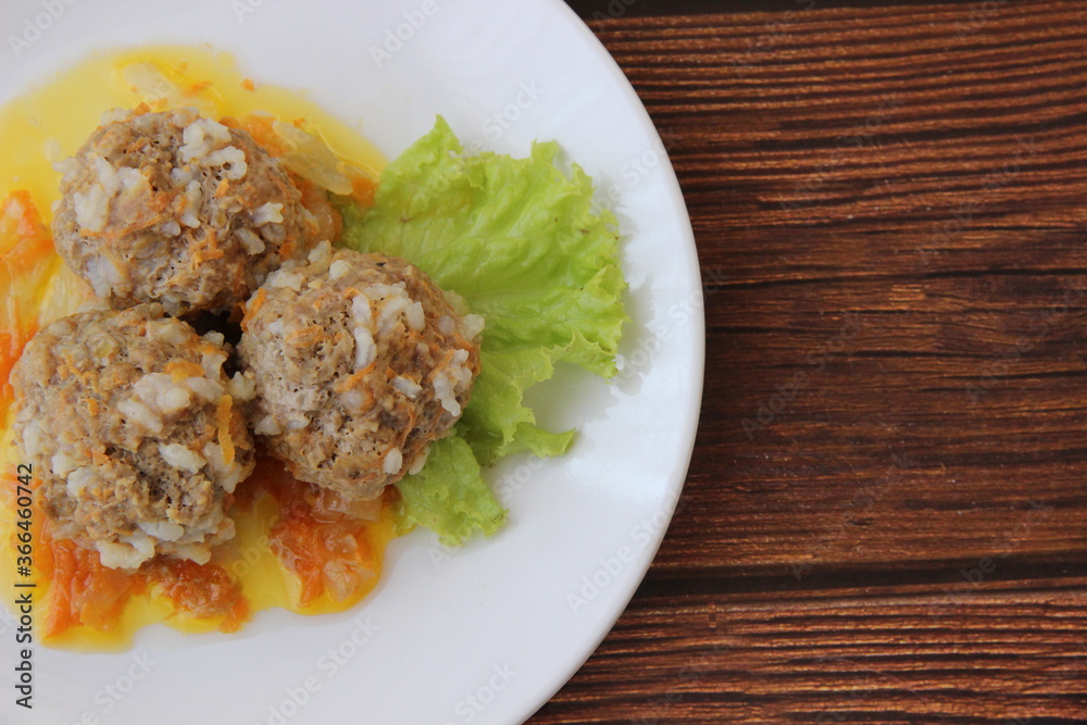 Meatballs with rice and carrots on a white plate and dark wooden boards Meatballs with rice and carrots on a white plate and dark wooden boards