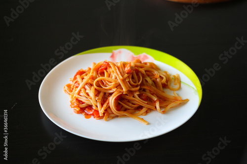 Pasta with vegetable sauce on a white porcelain plate on a black table.