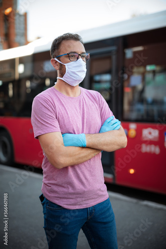 Man with medical protective mask and gloves waiting for the bus on a public transportation station.